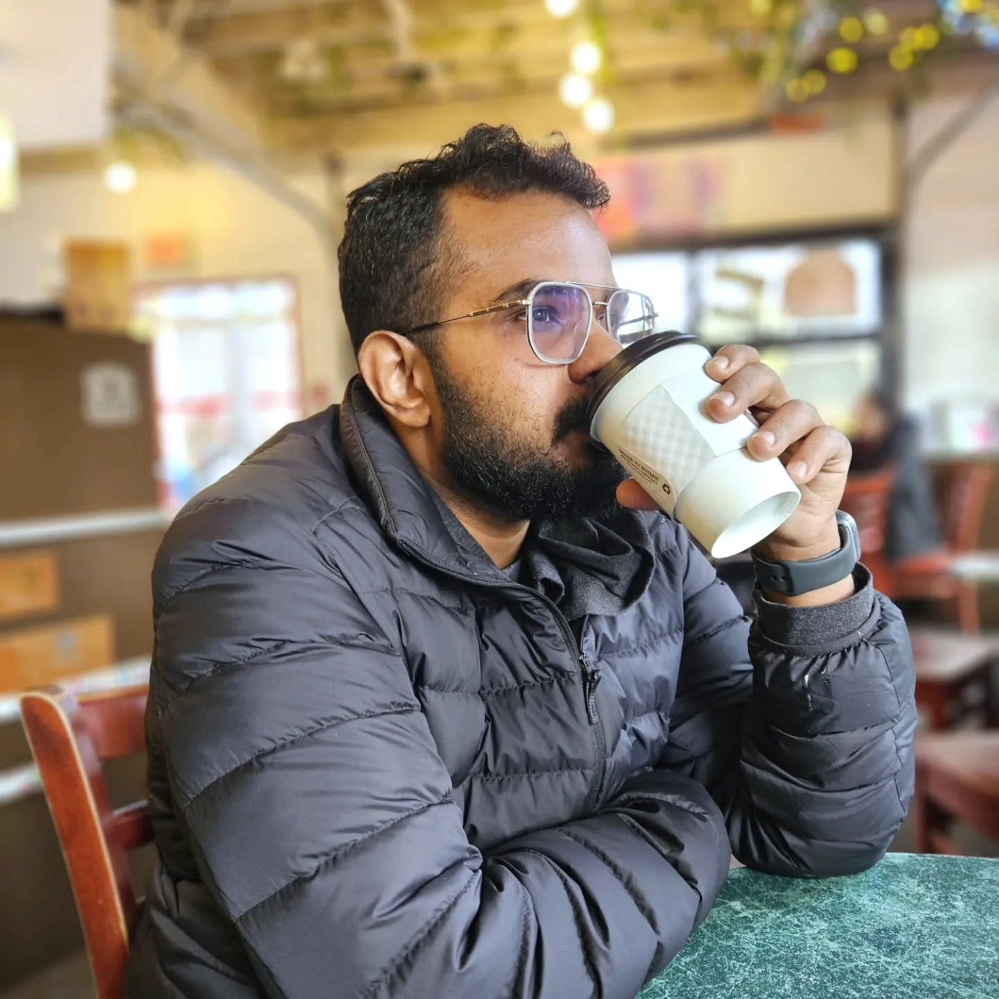 Jay sipping a takeaway coffee at a café table