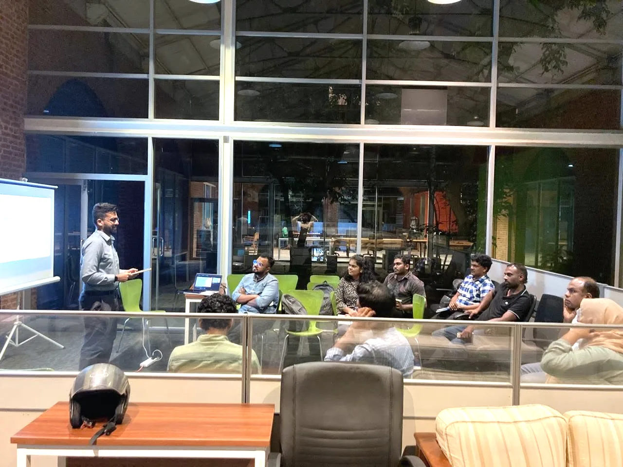 An evening book club session, with a presenter at the screen and members seated in a circle