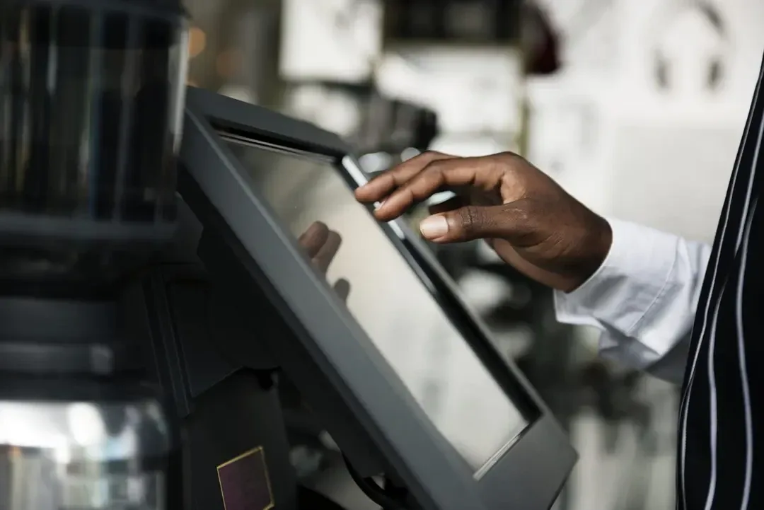 A hand tapping a touchscreen point-of-sale terminal at a shop counter