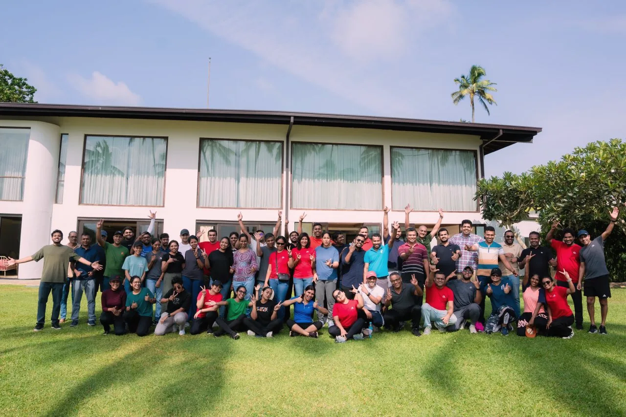 A large group of colleagues posing on a lawn in front of a hotel
